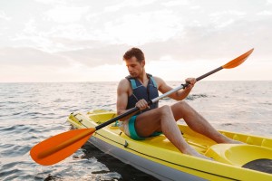 Image of young handsome man kayaking on lake sea in boat.